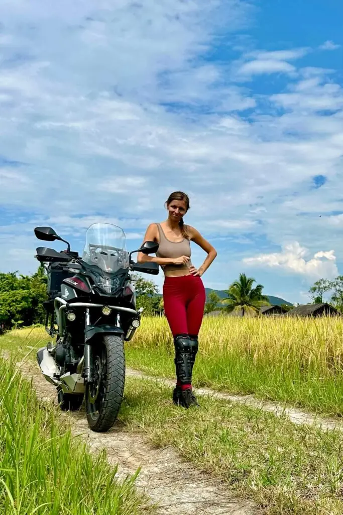 Baška standing next to her adventure motorcycle in a Northern Thailand rice field