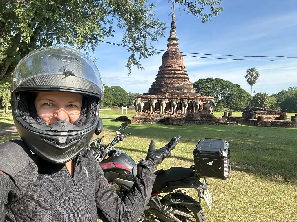 Female rider in a helmet in front of the Sukhothai temple ruins, motorbiking in Thailand
