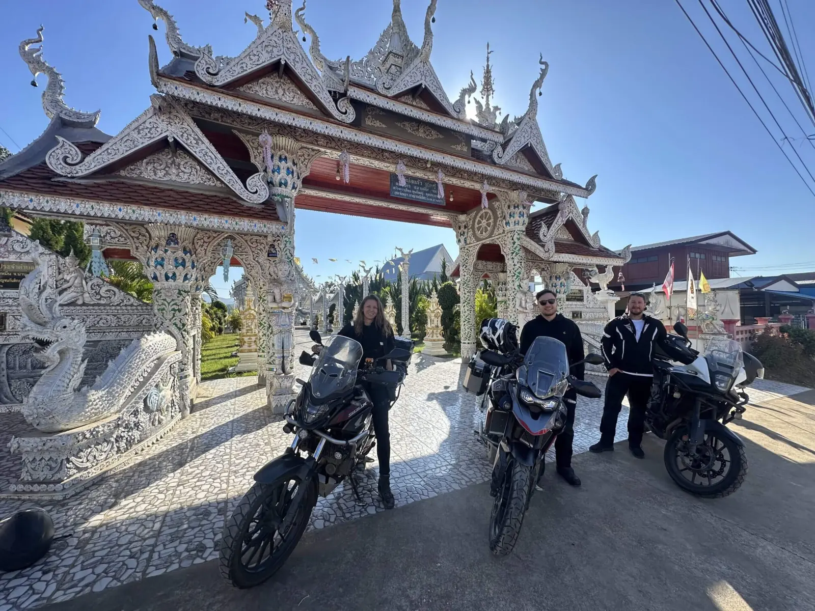 Women riders parked at an ornate temple gate during a guided motorcycle tour in Northern Thailand